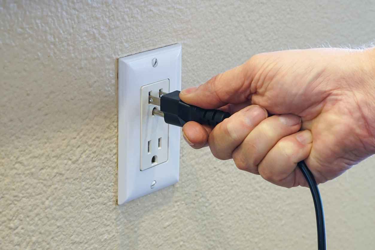 A man's hand plugging power cord into power