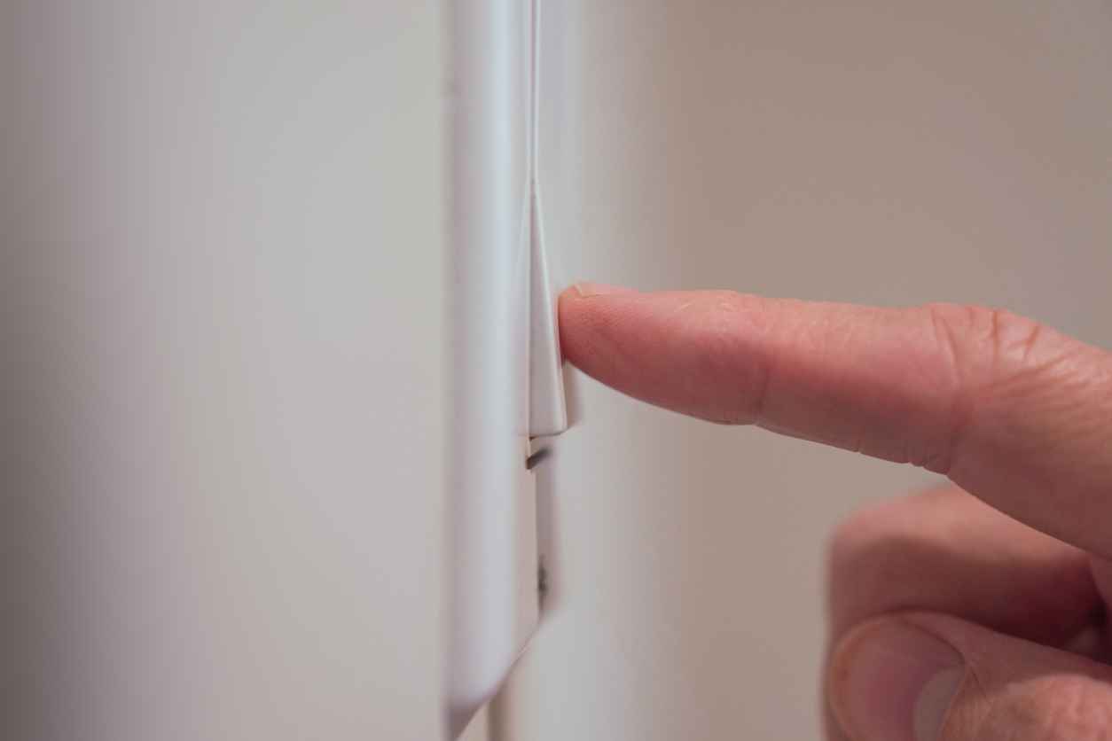Extreme closeup of finger of male hand pushing light switch on wall