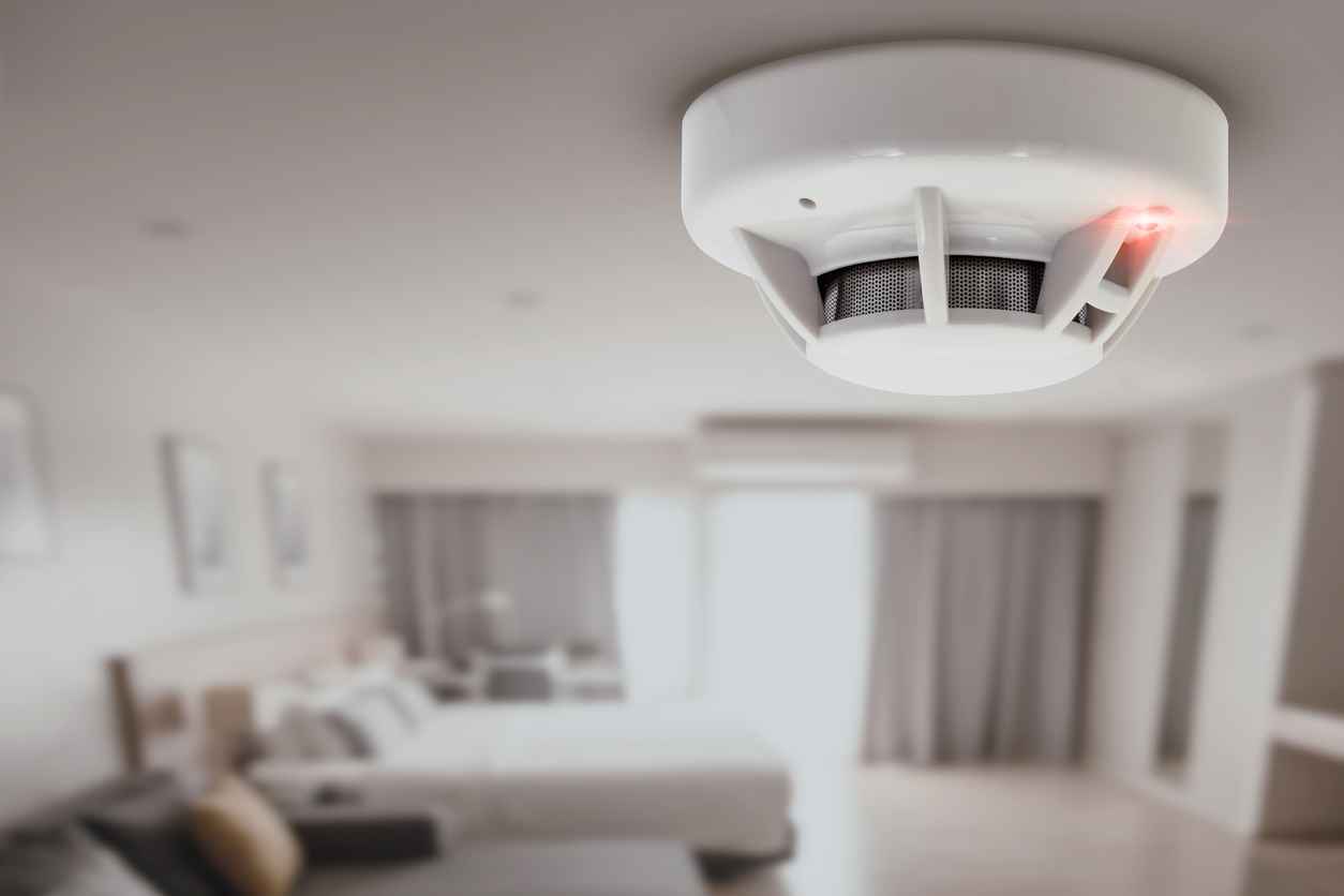 Close-up of a smoke detector blinking red in a bedroom