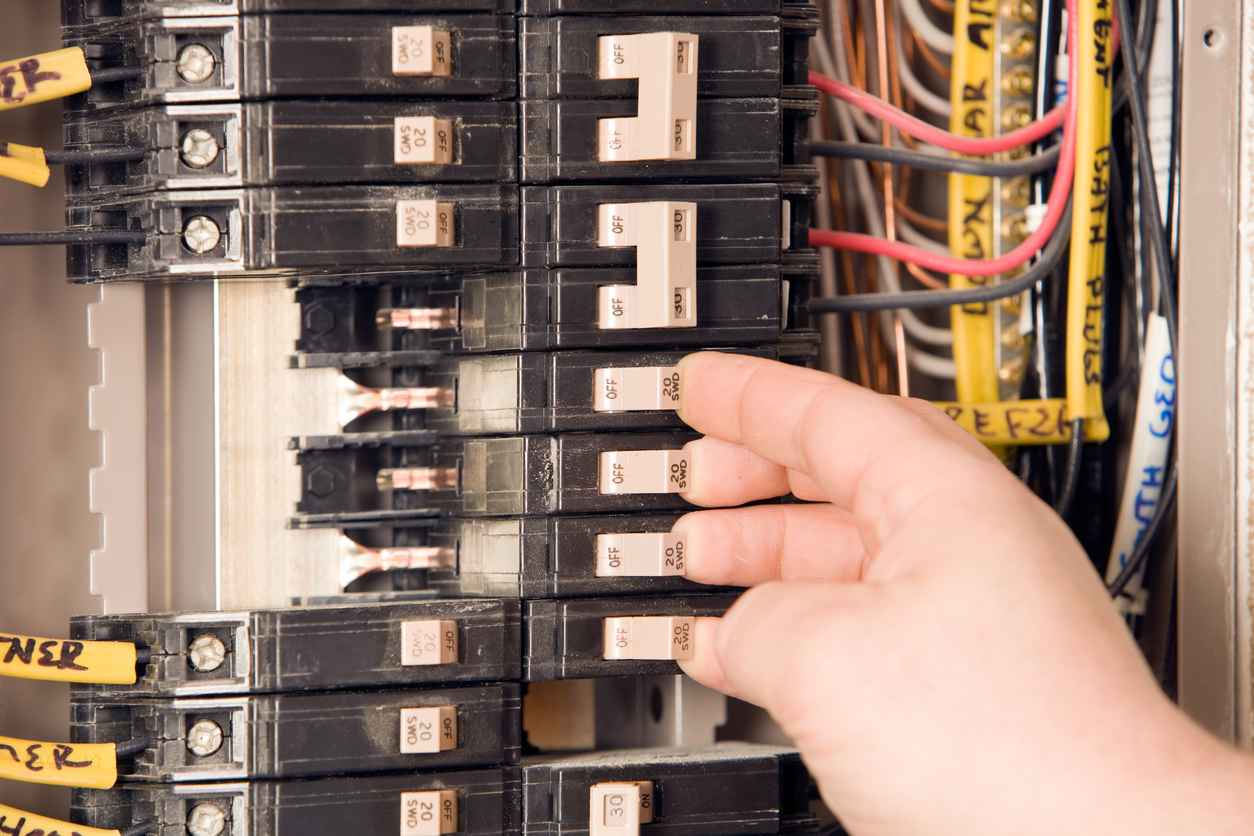 Electrician’s hand turning on circuit breakers on service panel