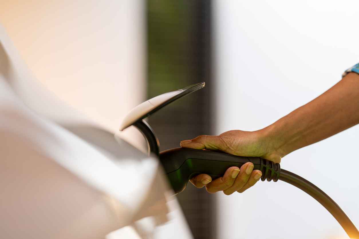 Woman hand charging electric car battery, holding plug close up