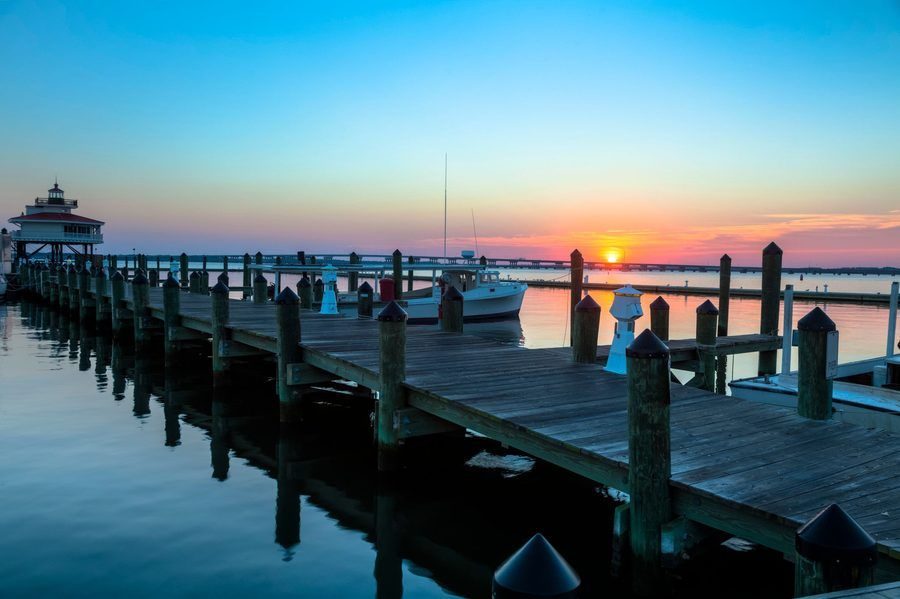 Sunset over a wooden pier with boats moored to posts, calm water reflecting the colorful sky.